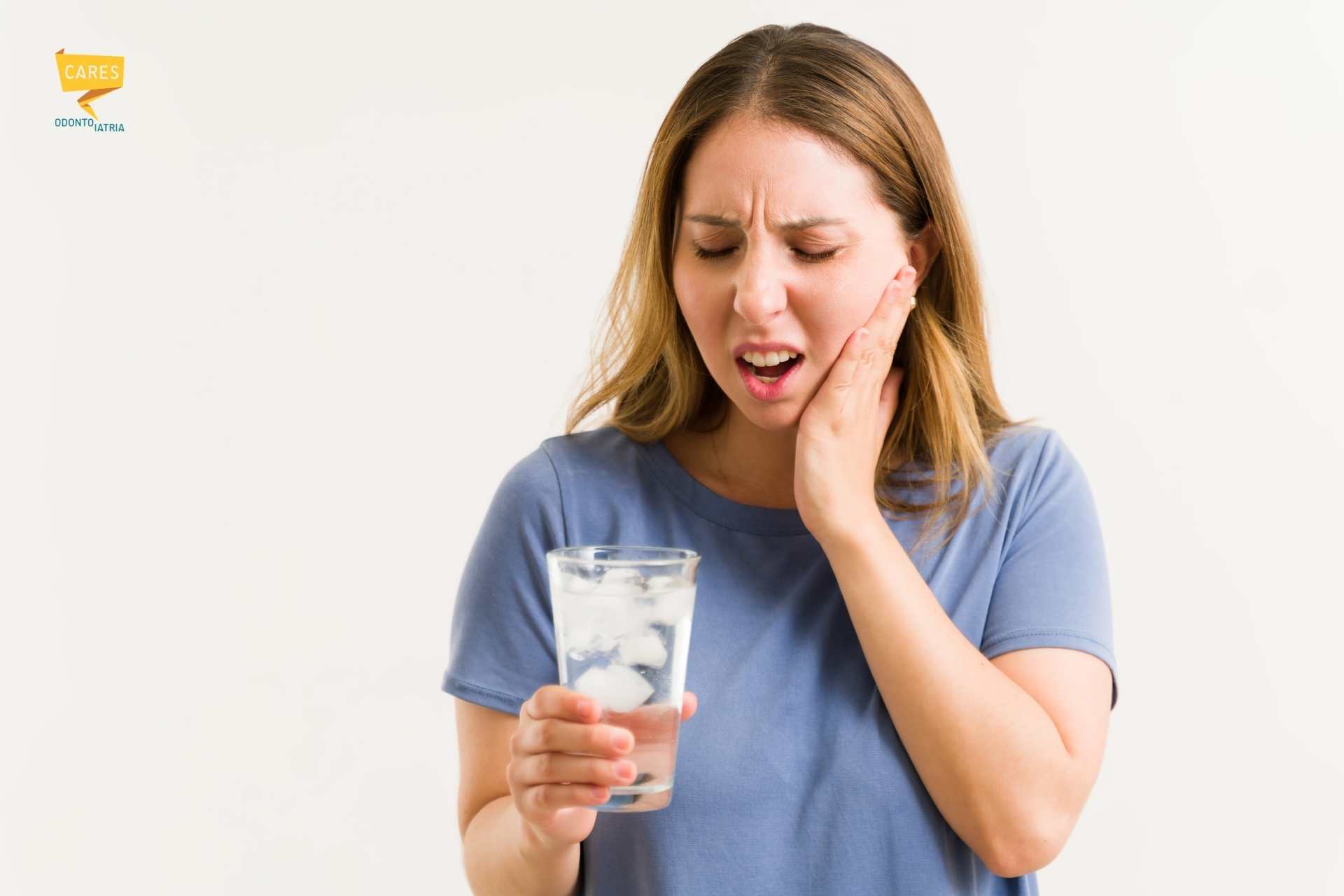 Donna che prova dolore ai denti mentre beve un bicchiere di acqua ghiacciata, sintomo tipico della sensibilità dentale e dei denti sensibili al freddo.