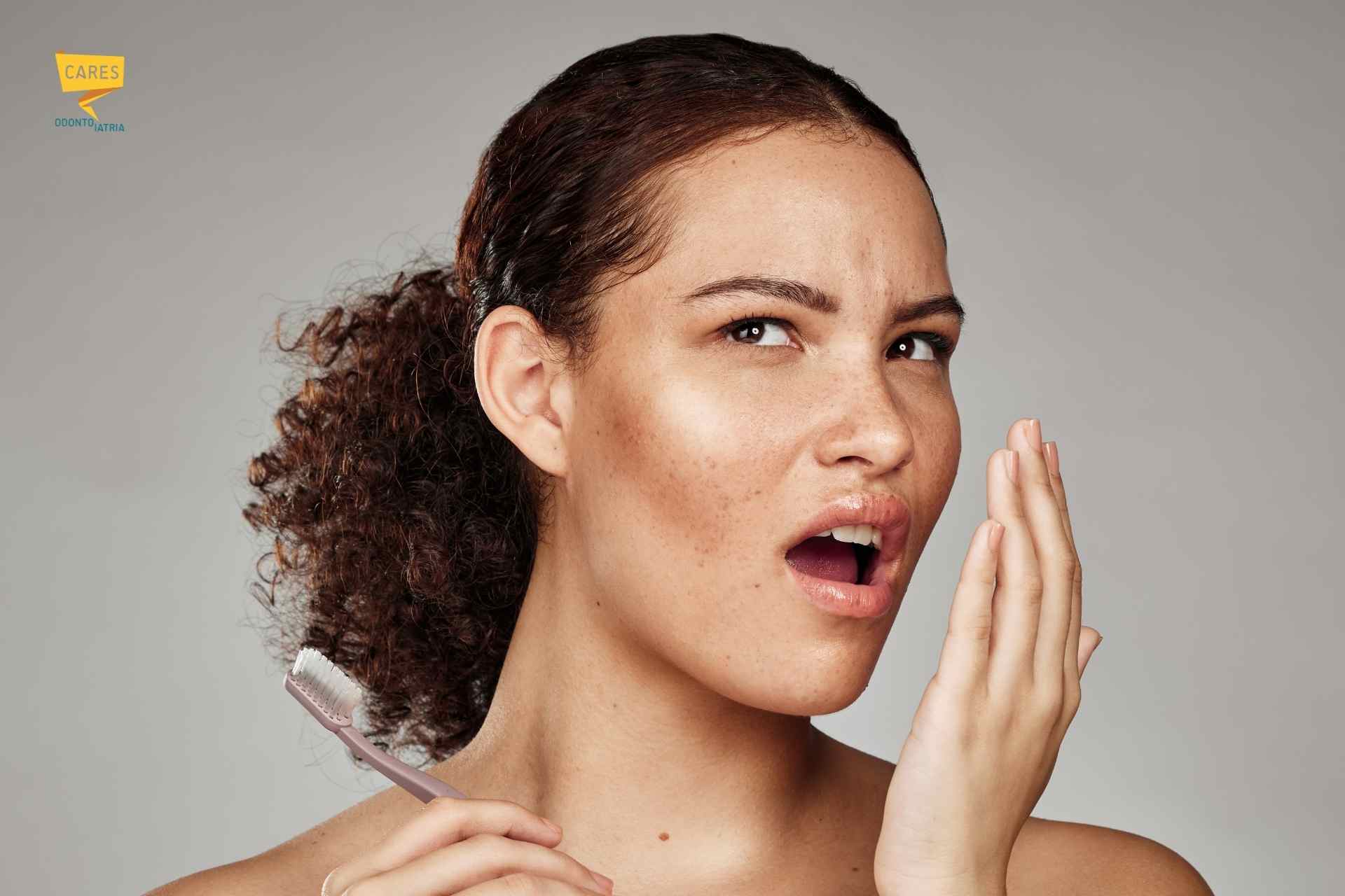 Donna che controlla l’alito con la mano mentre tiene uno spazzolino, simbolo di alito cattivo e igiene orale.