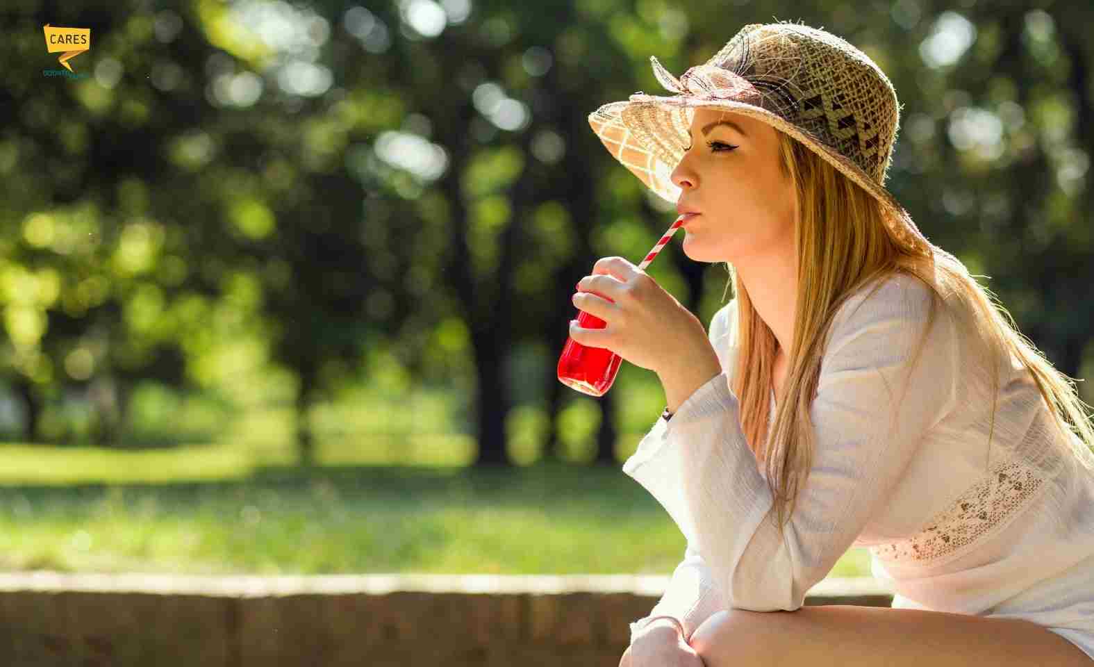 Donna all’aperto in estate beve una bibita fresca: caldo e disidratazione possono favorire bocca secca e problemi dentali.