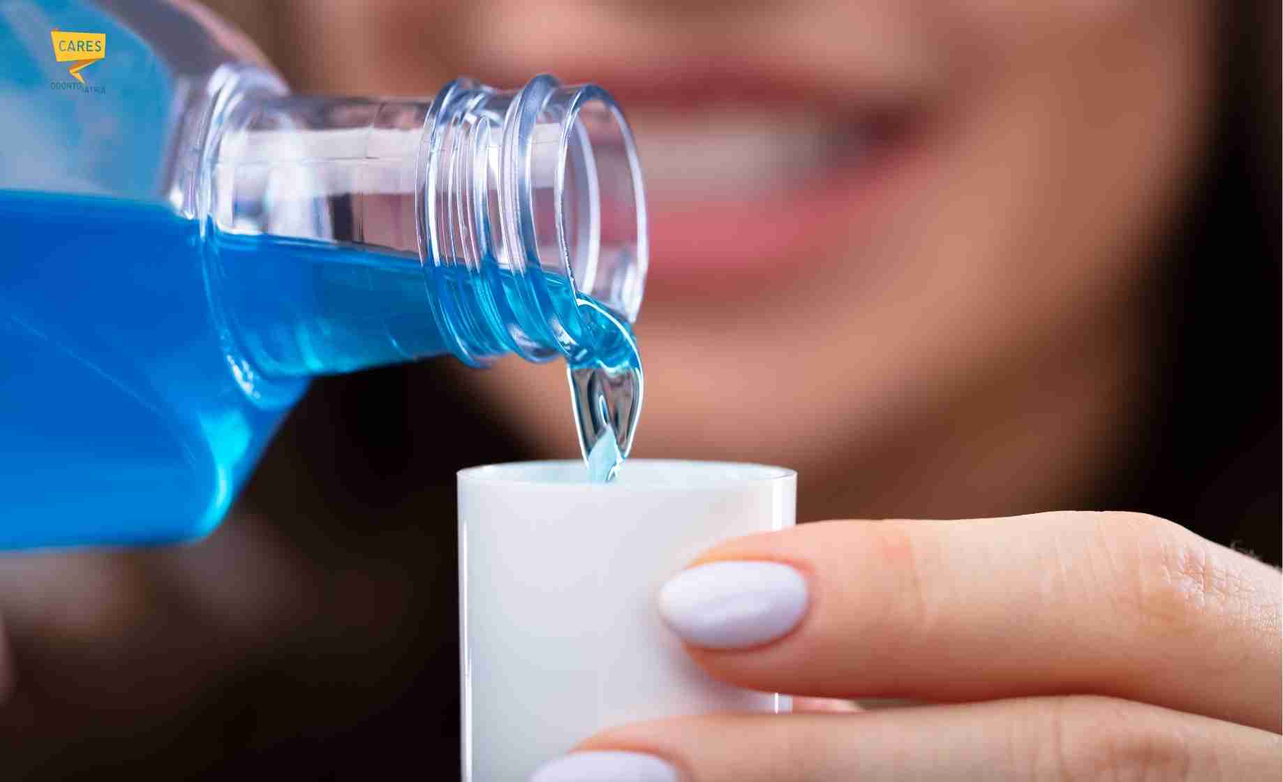 Persona che versa collutorio blu nel tappo per completare l’igiene orale quotidiana e aiutare le gengive infiammate